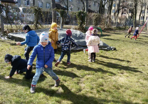 Widok na grupę bawiących się w ogrodzie przedszkolnym dzieci, które chwytają spadające bańki mydlane.